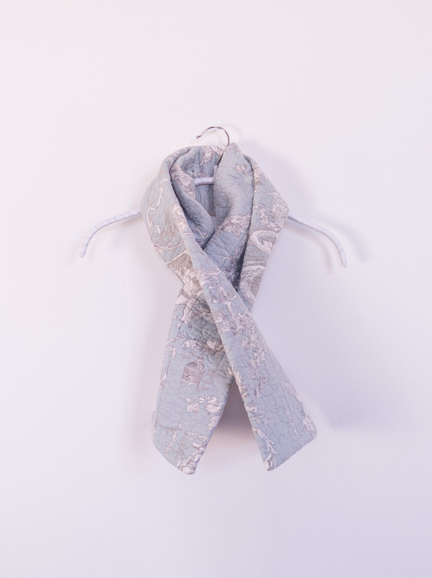 Handgefertigter „Heaven’s Stripe Club Scarf“ aus Baumwolle mit zartblauem Grund und cremefarbenem Engelmuster, auf einem Hacken drapiert.