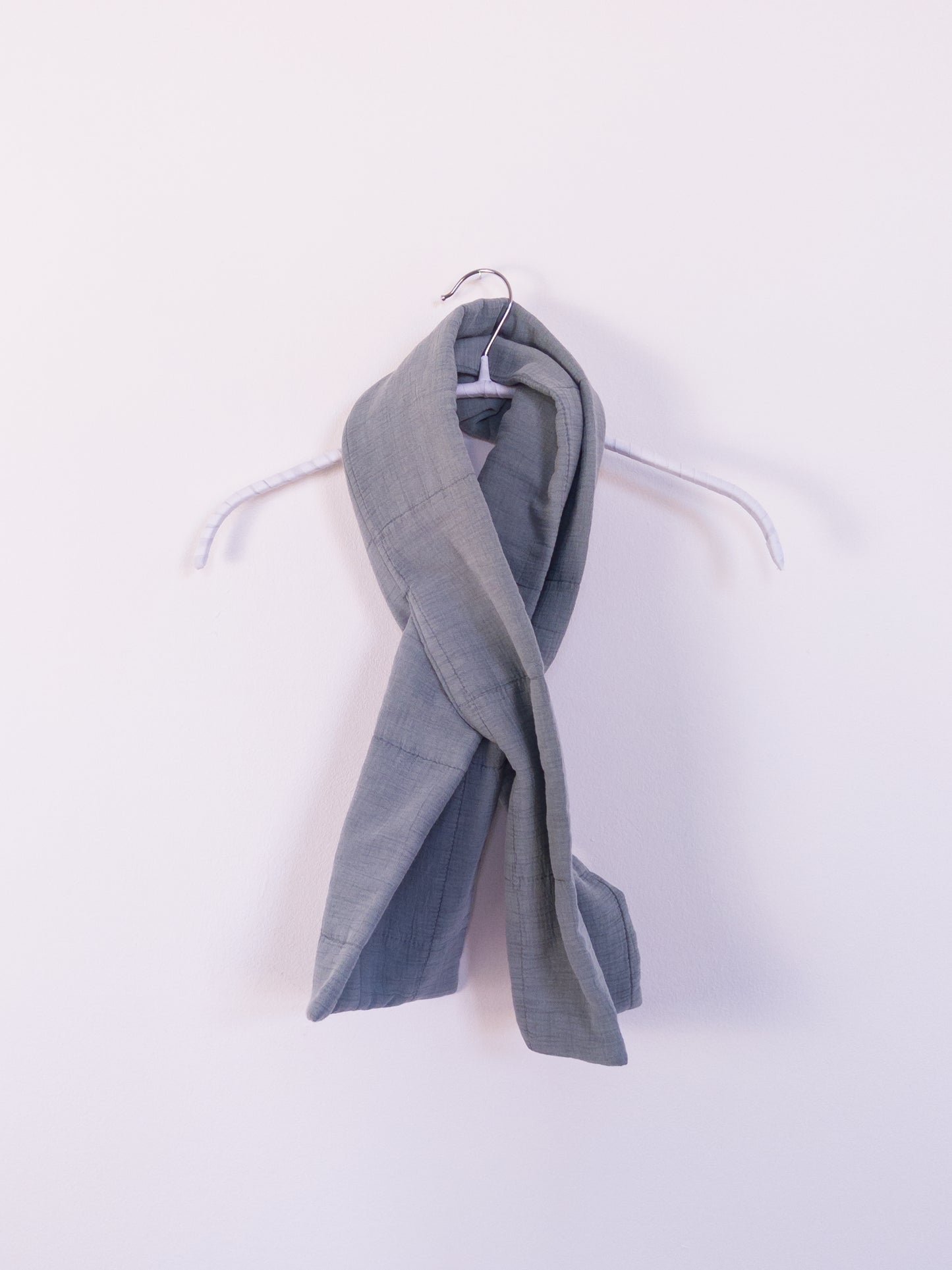 "Soft Spot Scarf" aus hellblauer, leicht gesteppten Musselindecke, auf einem Kleiderhaken gebunden.
