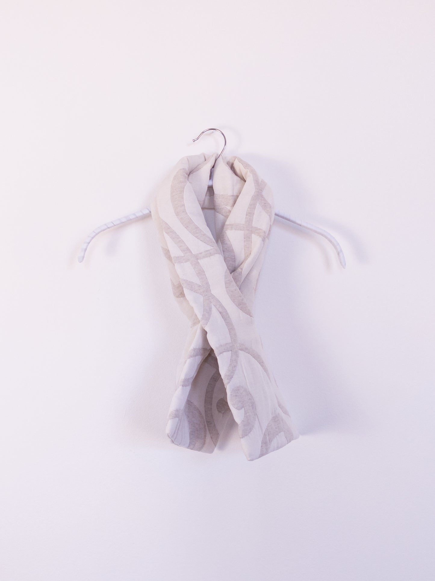 Handgefertigter „The Oatmeal Enthusiast Scarf“ aus cremefarbener Steppdecke, um einem Haken gebunden.