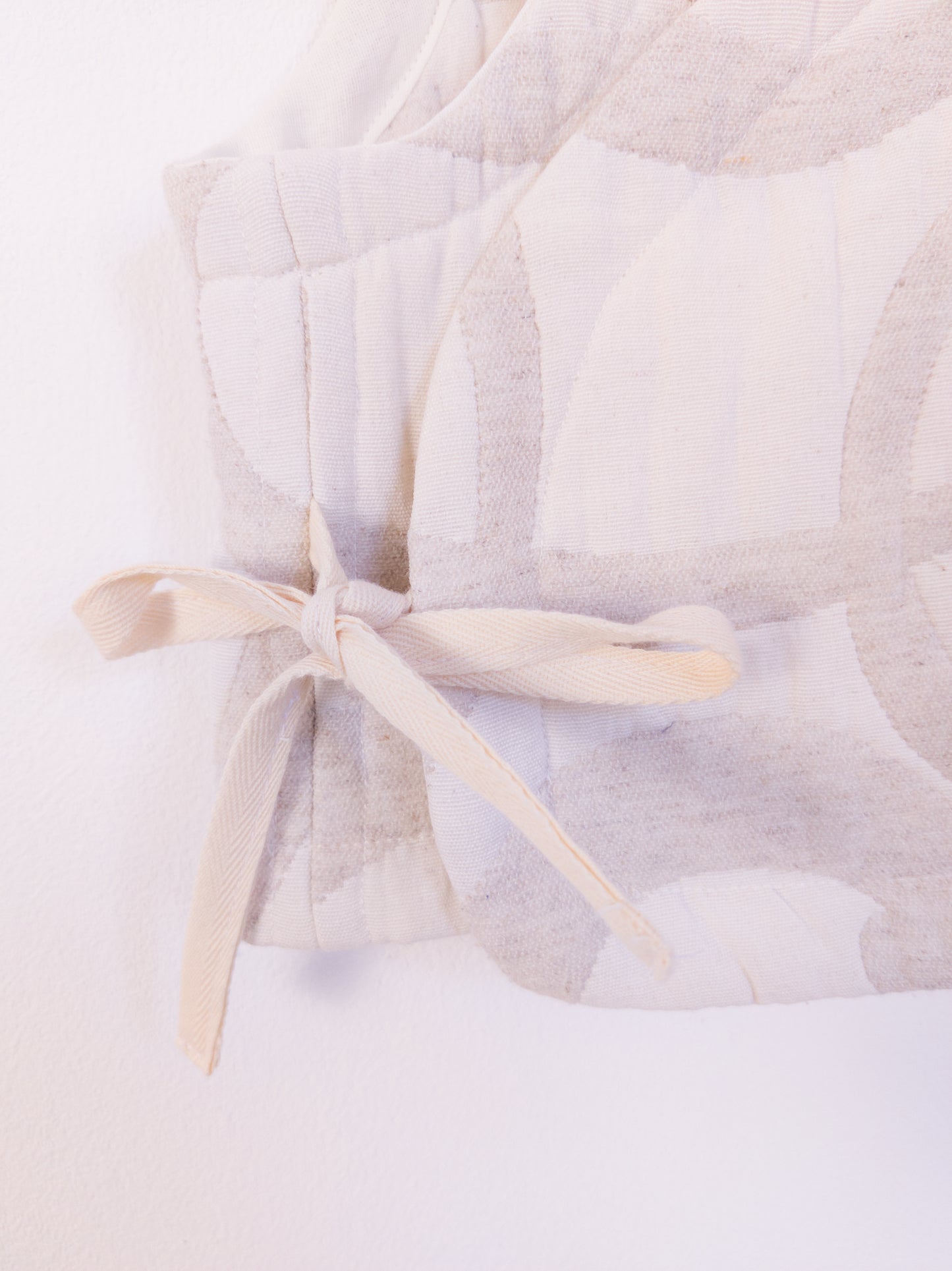 Detailansicht der „The Oatmeal Enthusiast Vest“ aus weicher, beigefarbener Kunstfaser mit feinen Schlingen, gebunden mit beiger Schleife an der Seite.