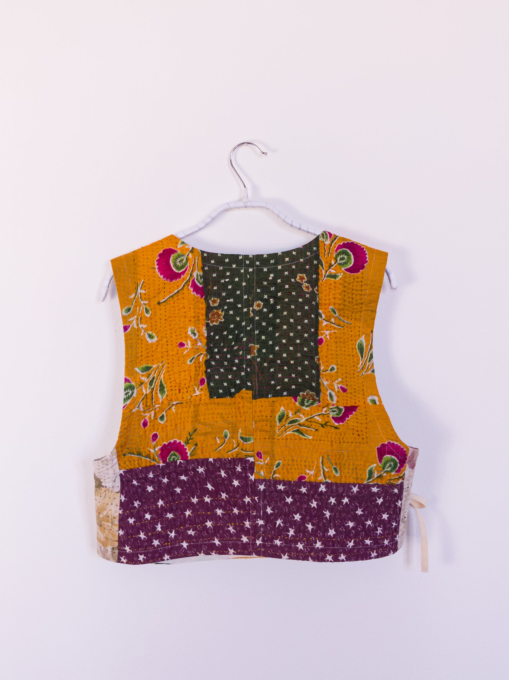 Rückansicht der „Flower Patch Club Vest“, zeigt das detailreiche Patchwork aus lila, orange, cremefarbenen und grünen Stoffen.