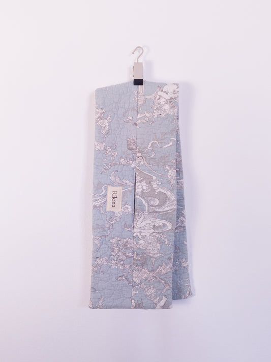 Der „Heaven’s Stripe Club Scarf“ mit himmlischen Motiven – Engel, Vogelkäfige und feine Weinranken, auf einem Haken hängend.