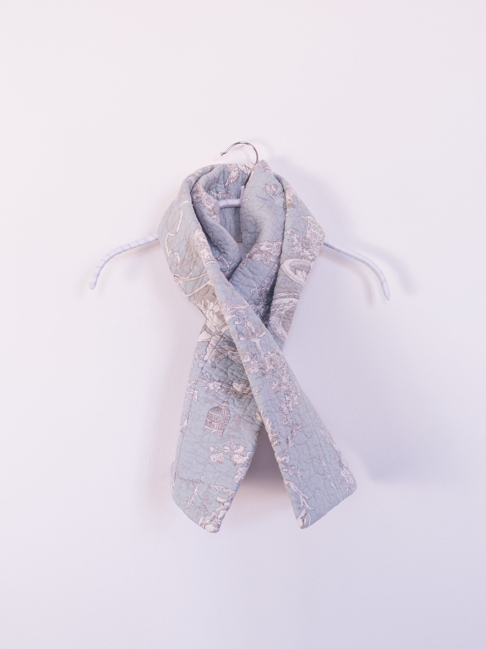 Handgefertigter „Heaven’s Stripe Club Scarf“ aus Baumwolle mit zartblauem Grund und cremefarbenem Engelmuster, auf einem Hacken drapiert.