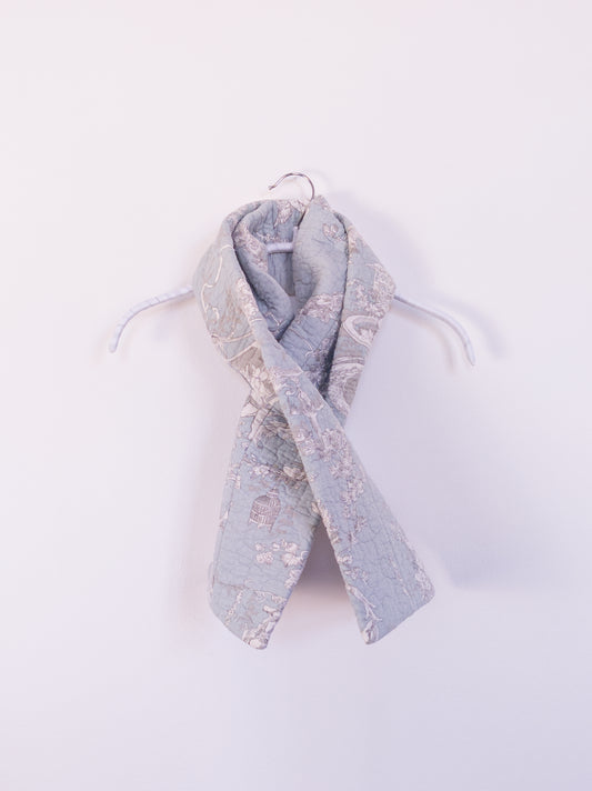 Handgefertigter „Heaven’s Stripe Club Scarf“ aus Baumwolle mit zartblauem Grund und cremefarbenem Engelmuster, auf einem Hacken drapiert.