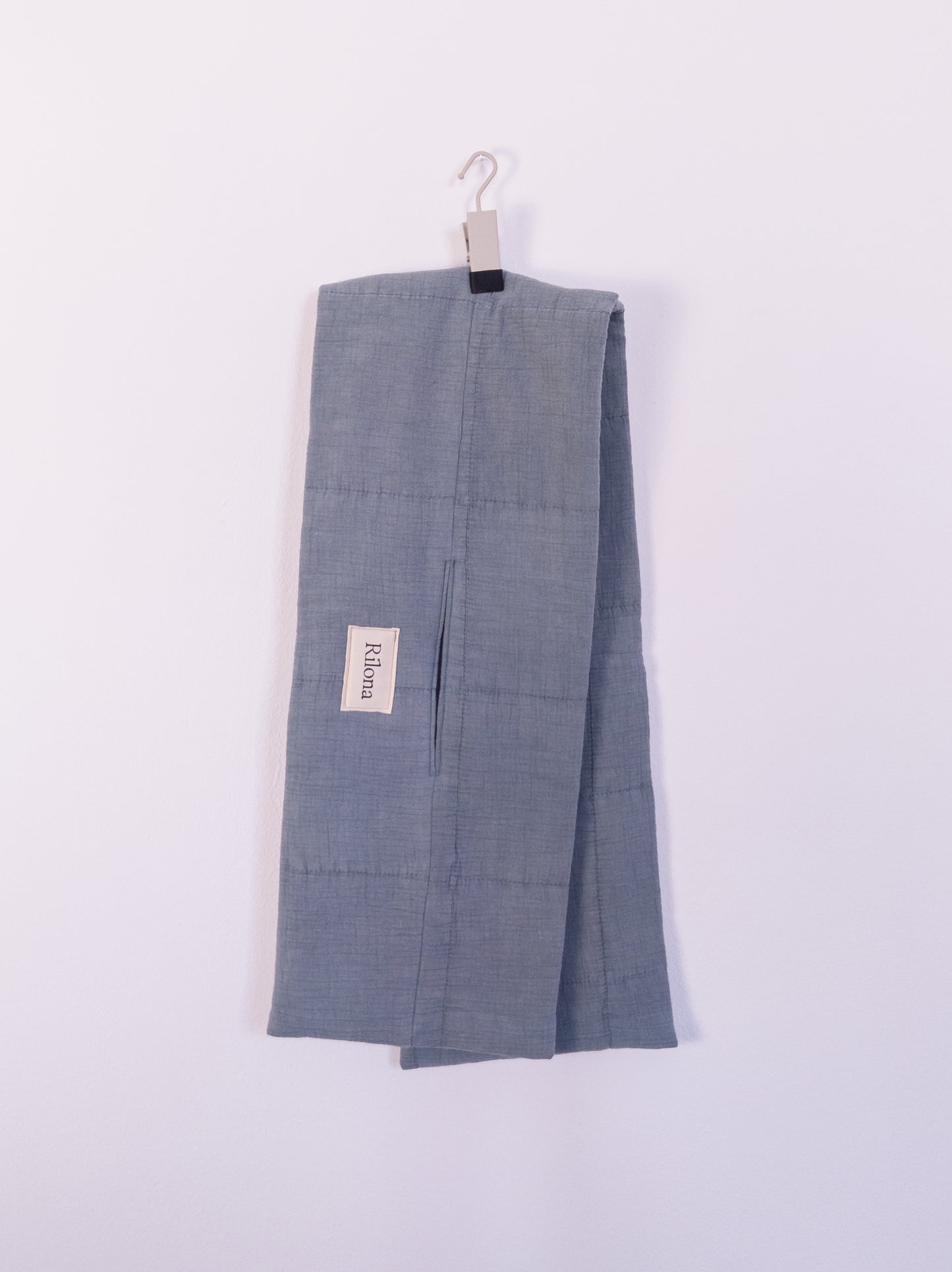 "Soft Spot Scarf" aus hellblauer Musselindecke mit quadratischer Steppung, auf einem Haken hängend.