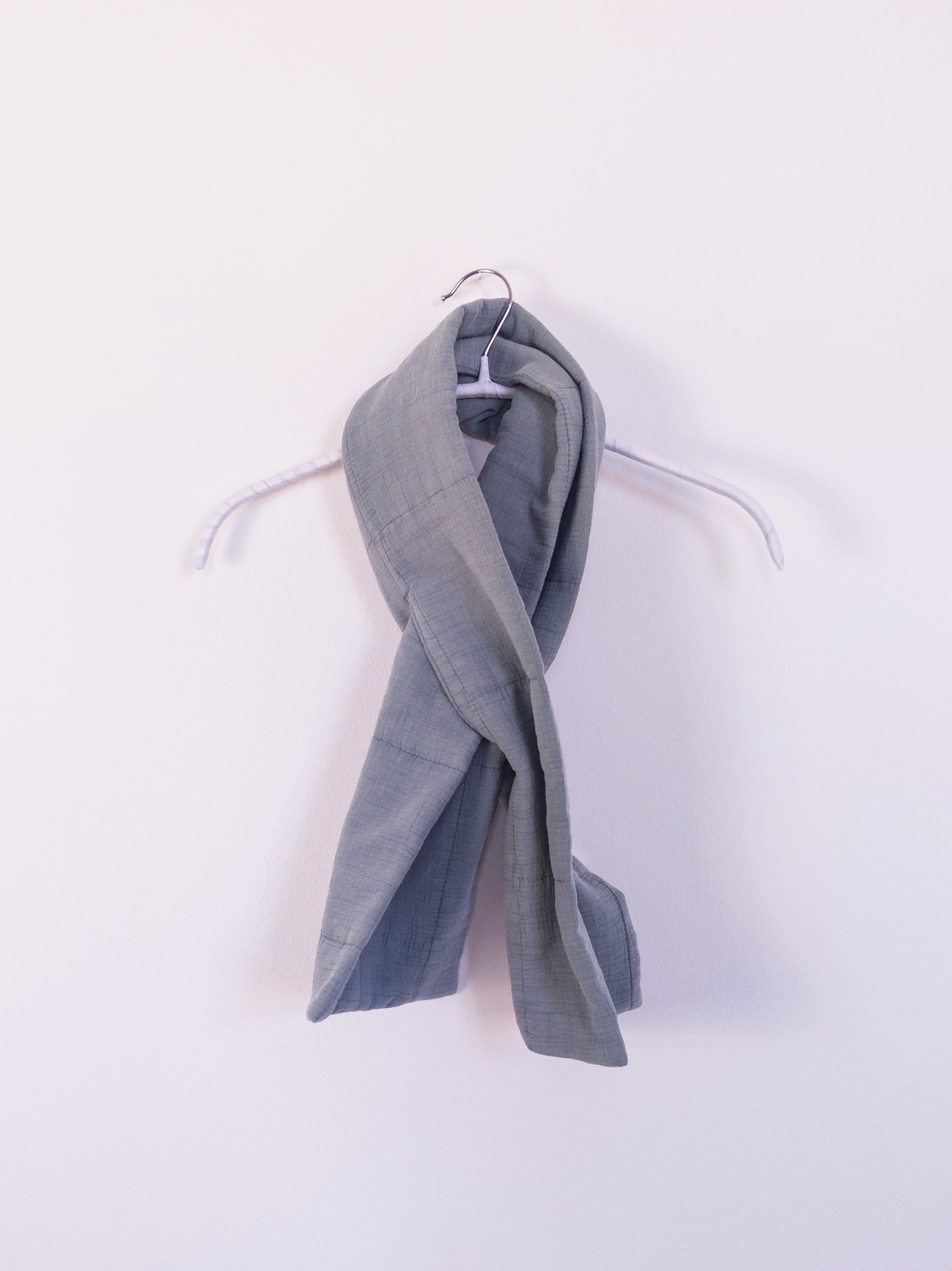 "Soft Spot Scarf" aus hellblauer, leicht gesteppten Musselindecke, auf einem Kleiderhaken gebunden.