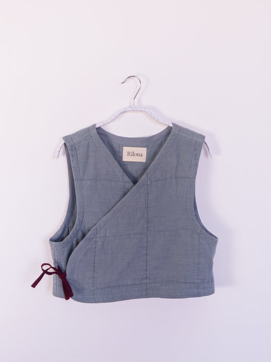 Vorderansicht der handgefertigten „Soft Spot Vest“ aus blauer Musselindecke mit quadratischer Steppung, gebunden mit roter Schleife.