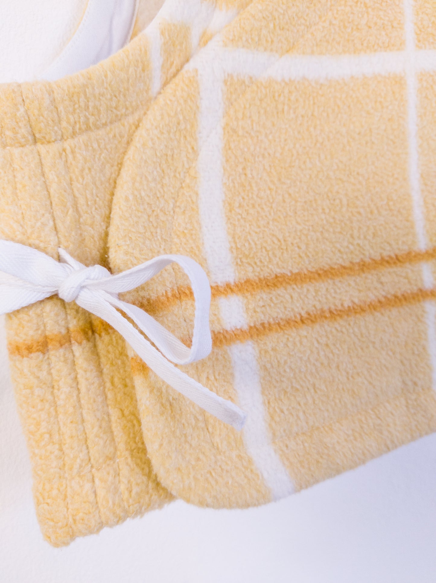 Detailaufnahme der „Sunny Side Up Vest“, zeigt die flauschige Textur und das leuchtend gelb-karierte Muster.