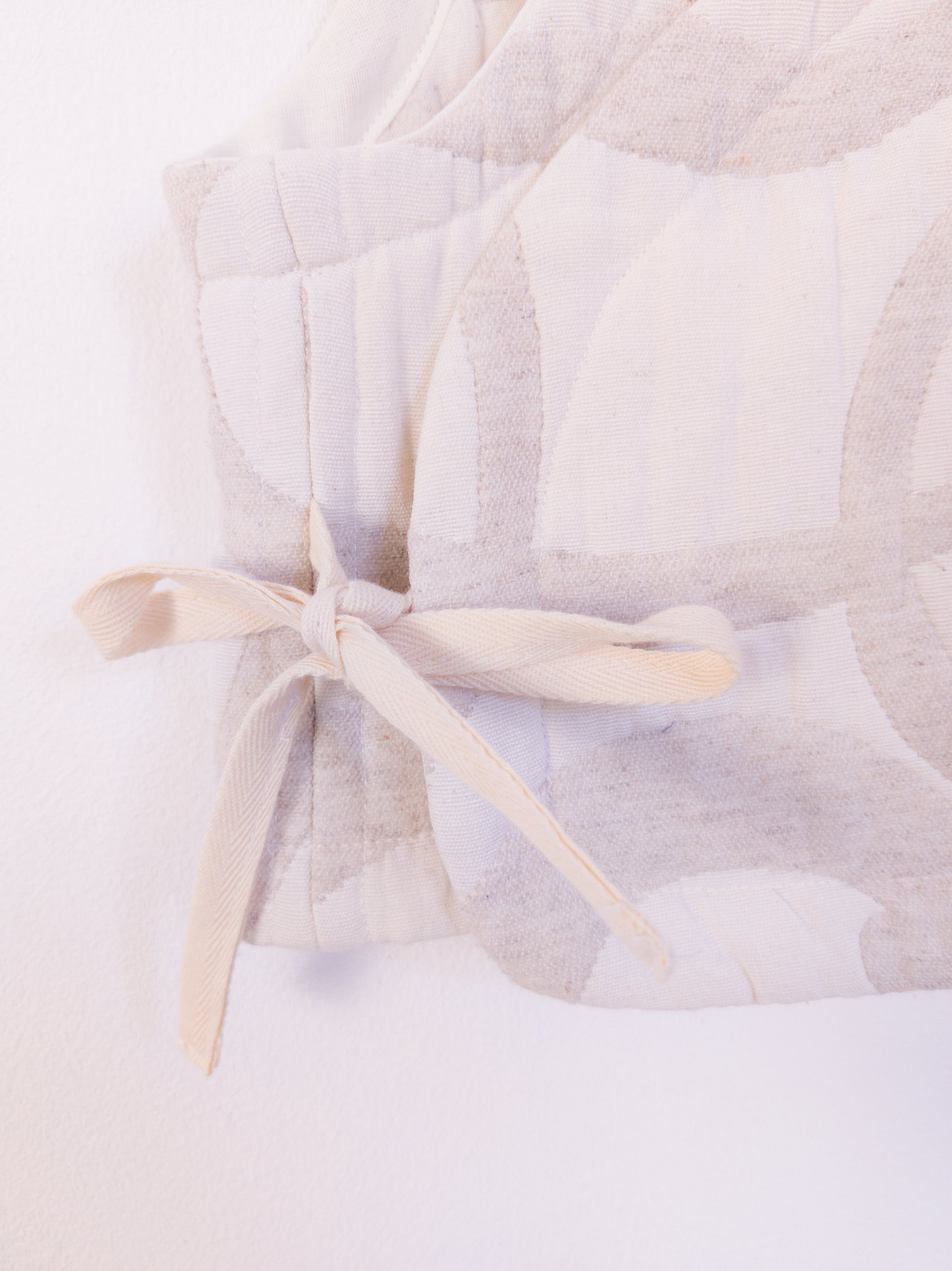 Detailansicht der „The Oatmeal Enthusiast Vest“ aus weicher, beigefarbener Kunstfaser mit feinen Schlingen, gebunden mit beiger Schleife an der Seite.