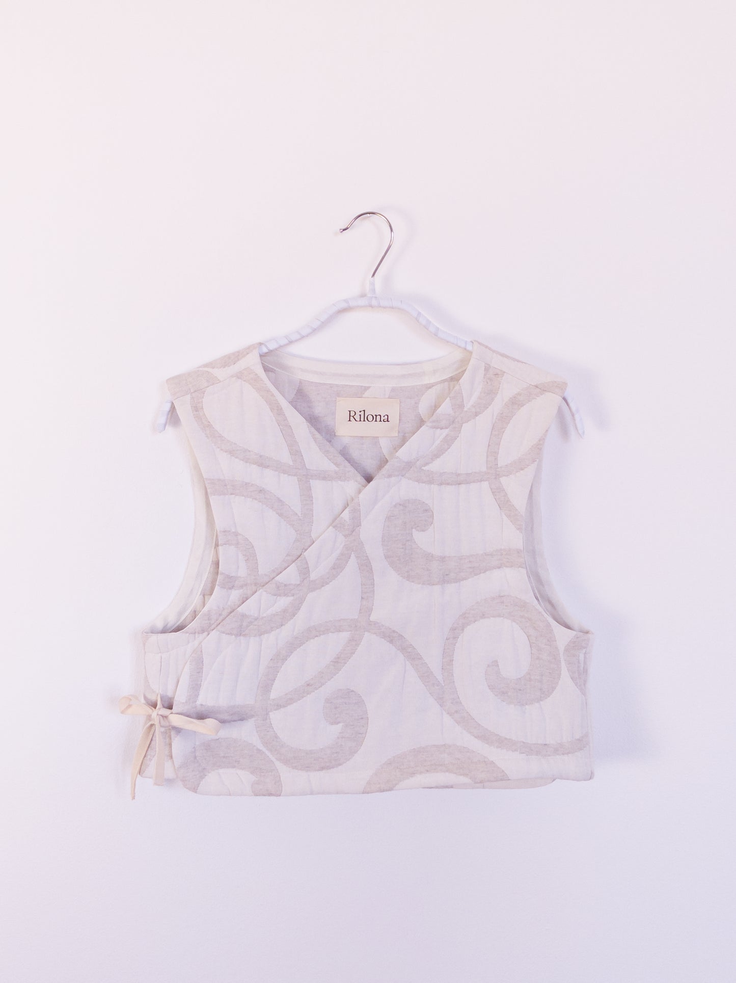 Vorderansicht der handgefertigten „The Oatmeal Enthusiast Vest“ aus beiger Steppdecke mit feinen Schlingen, auf einem Haken hängend.