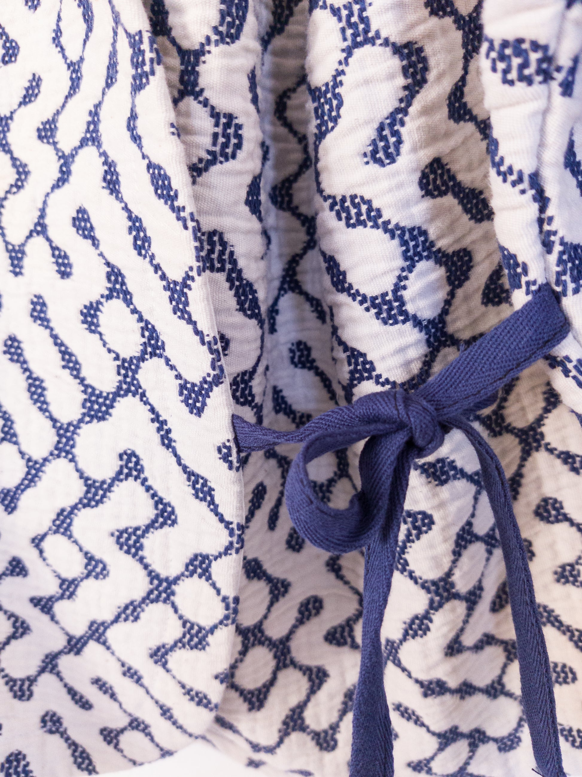 Datailansicht der handgefertigten „The Orb Awakens Jacket“ aus Baumwolle, blau mit weißem kreisförmigem Muster, gebunden mit blauer Schleife.