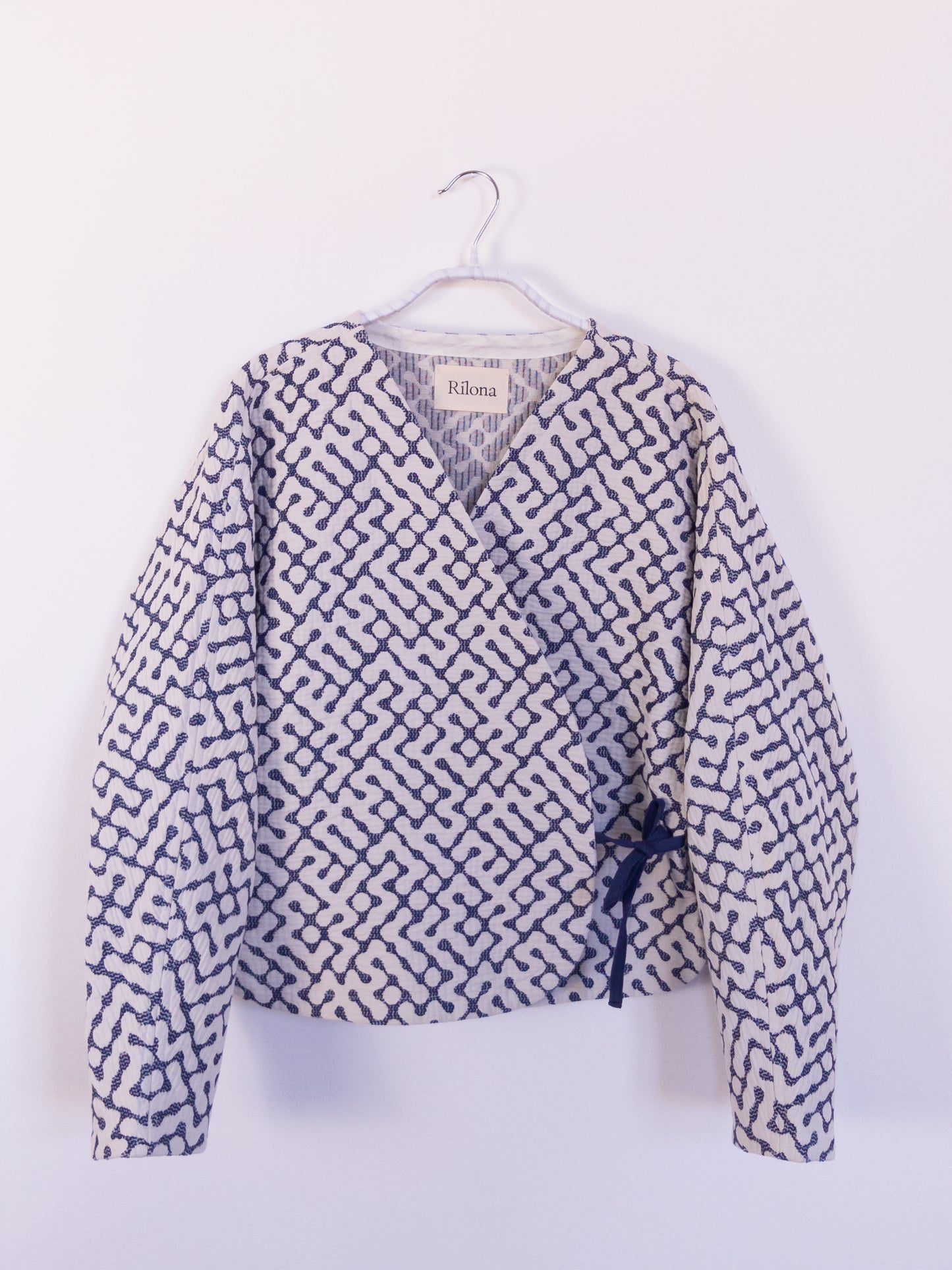 Vorderansicht der handgefertigten „The Orb Awakens Jacket“ aus Baumwolle, blau mit weißem kreisförmigem Muster, auf einem Haken hängend.