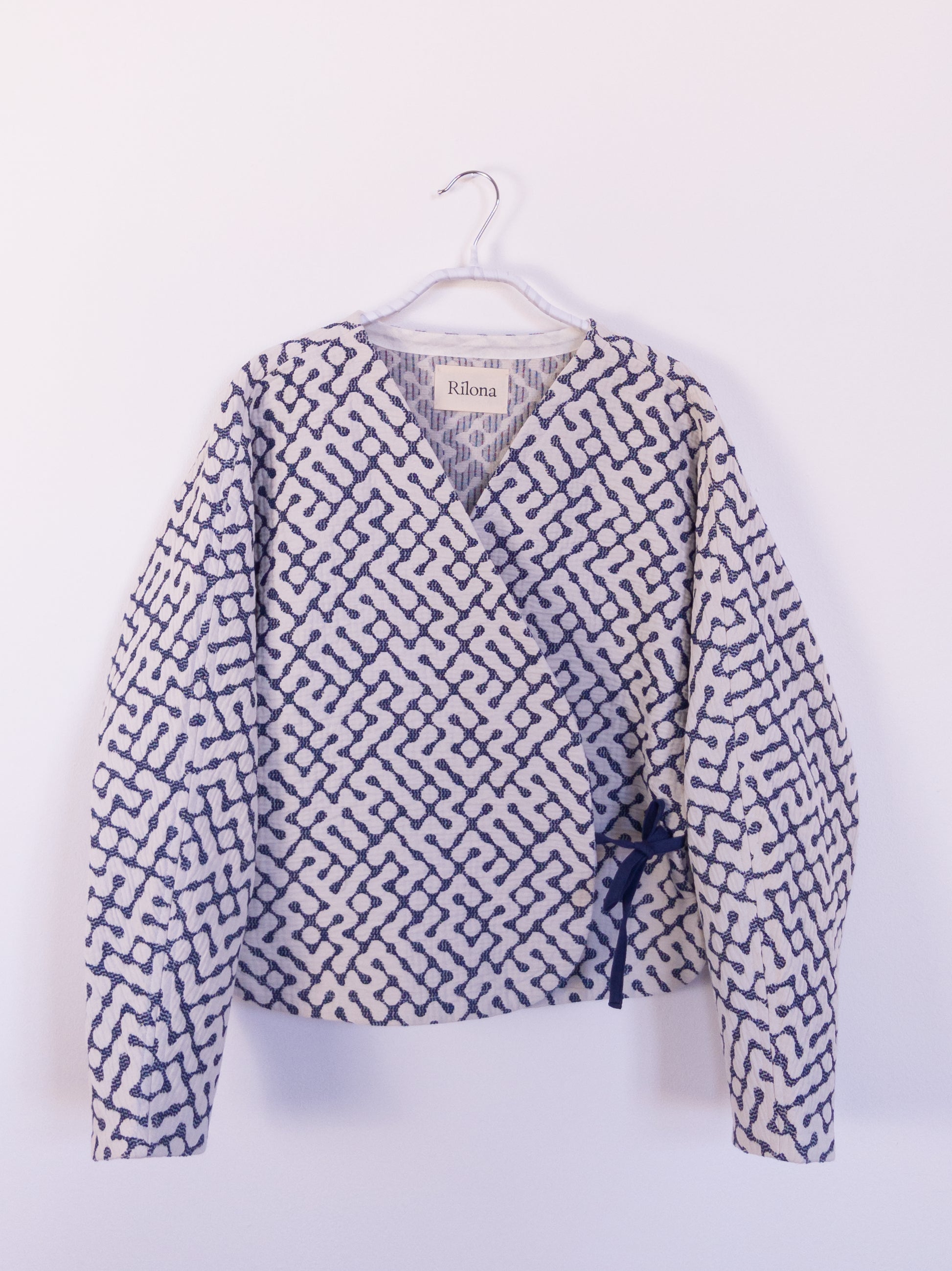 Vorderansicht der handgefertigten „The Orb Awakens Jacket“ aus Baumwolle, blau mit weißem kreisförmigem Muster, auf einem Haken hängend.