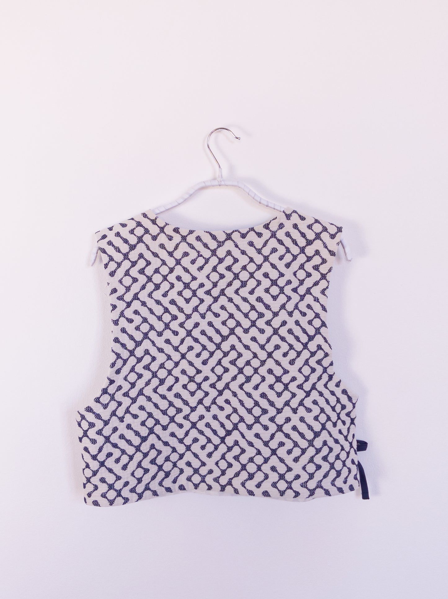 Rückansicht der handgefertigten „The Orb Awakens Vest“ aus Baumwolle, blau mit weißem kreisförmigem Muster, auf einem Haken hängend.