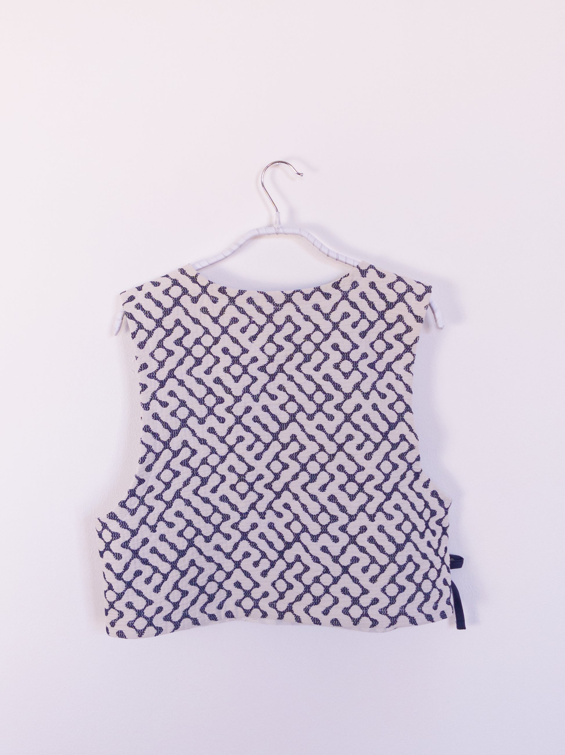 Rückansicht der handgefertigten „The Orb Awakens Vest“ aus Baumwolle, blau mit weißem kreisförmigem Muster, auf einem Haken hängend.