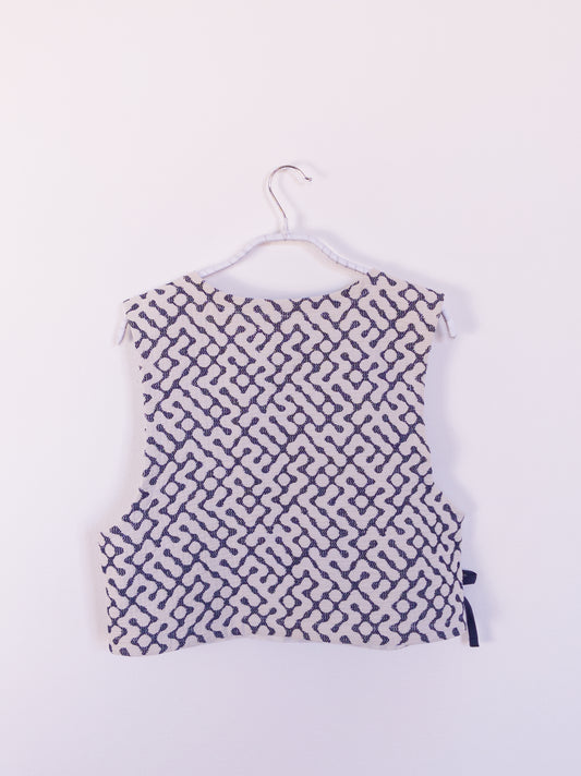 Rückansicht der handgefertigten „The Orb Awakens Vest“ aus Baumwolle, blau mit weißem kreisförmigem Muster, auf einem Haken hängend.