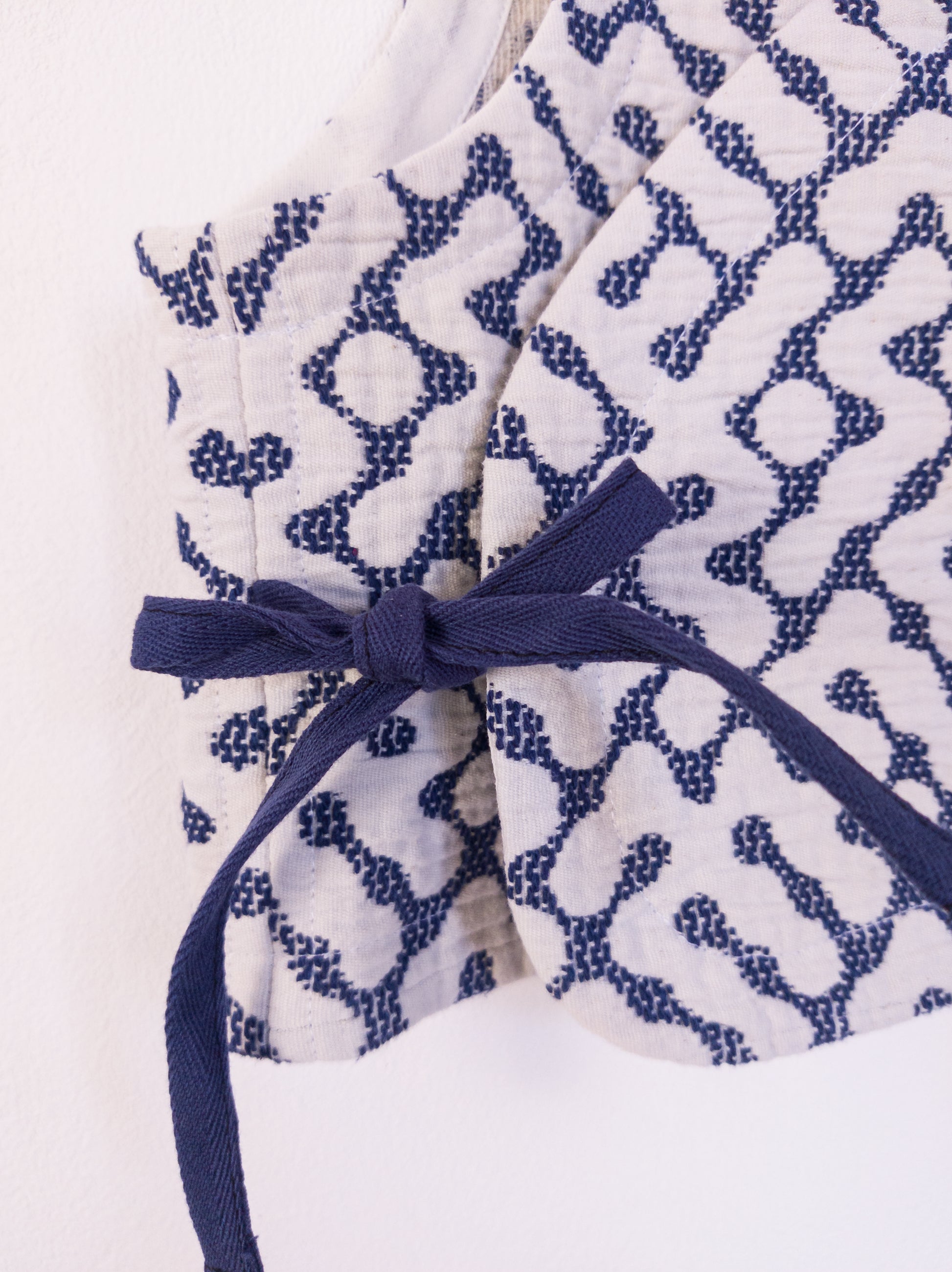 Detailansicht der handgefertigten „The Orb Awakens Vest“ aus Baumwolle in Blau mit weißem kreisförmigem Muster, gebunden mit blauer Schleife.