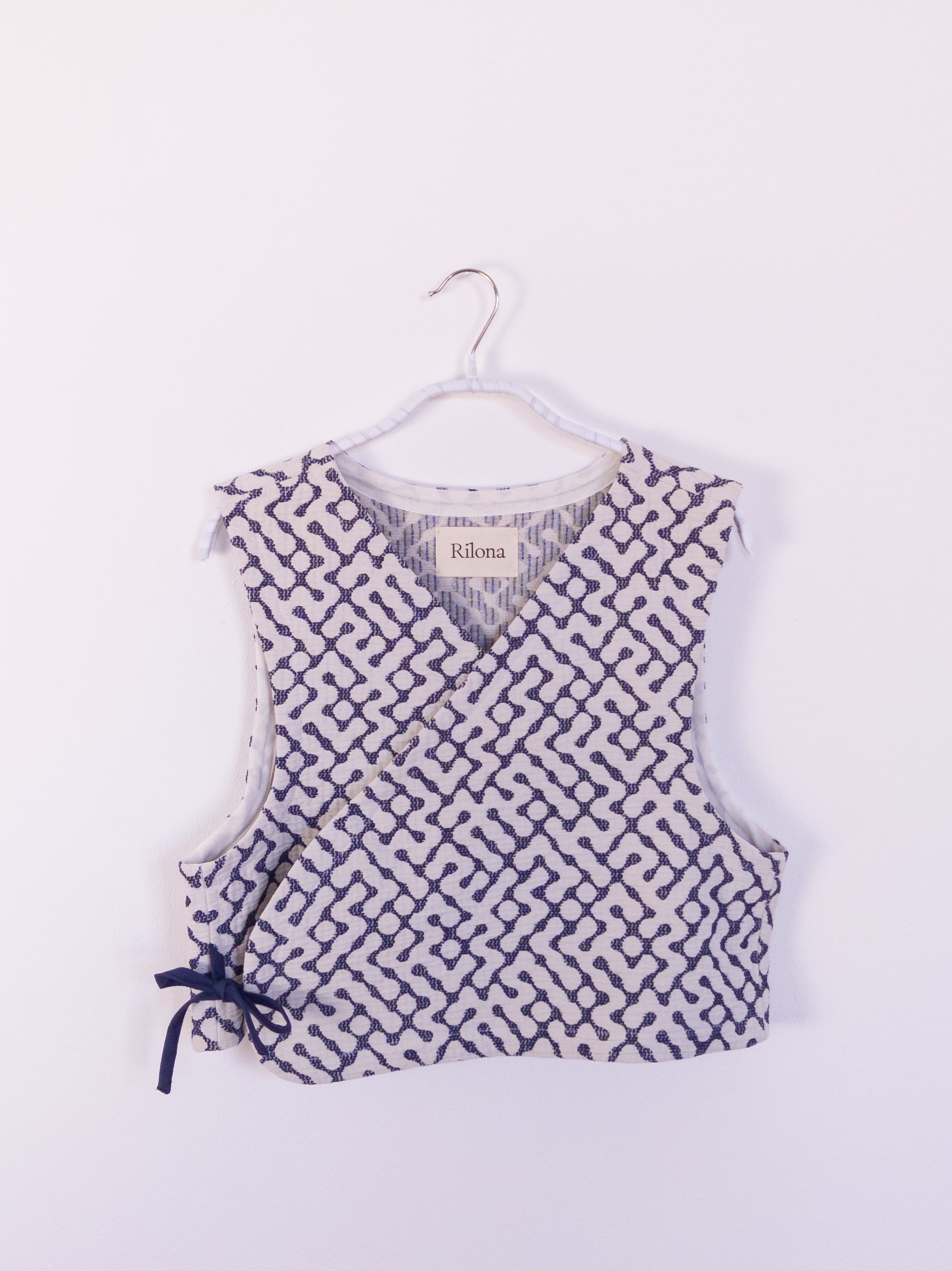 Vorderansicht der handgefertigten „The Orb Awakens Vest“ aus Baumwolle, blau mit weißem kreisförmigem Muster, auf einem Haken hängend.