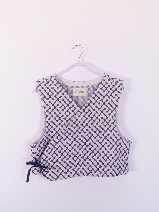 Vorderansicht der handgefertigten „The Orb Awakens Vest“ aus Baumwolle, blau mit weißem kreisförmigem Muster, auf einem Haken hängend.